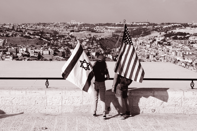 Two individuals standing with a US Flag and a flag of Israel