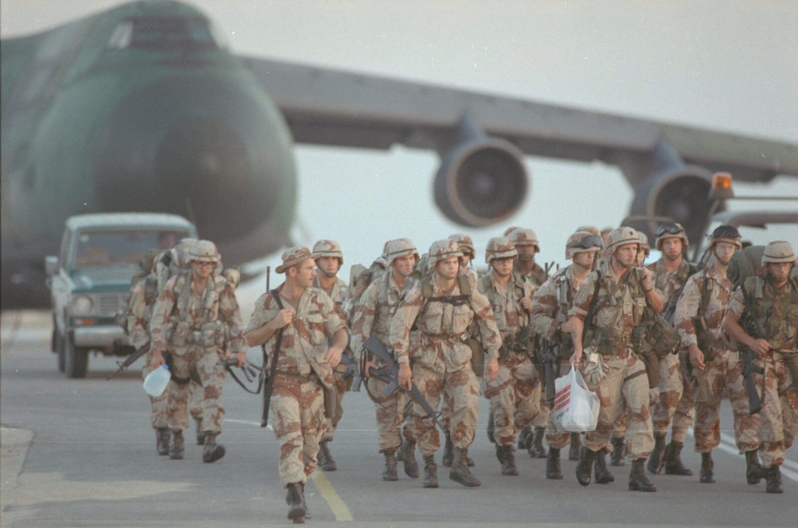 US troops in desert camouflage disembark near a military transport aircraft during a foreign deployment