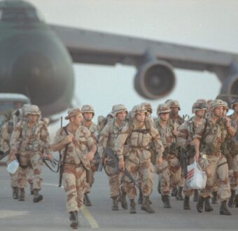 US troops in desert camouflage disembark near a military transport aircraft during a foreign deployment