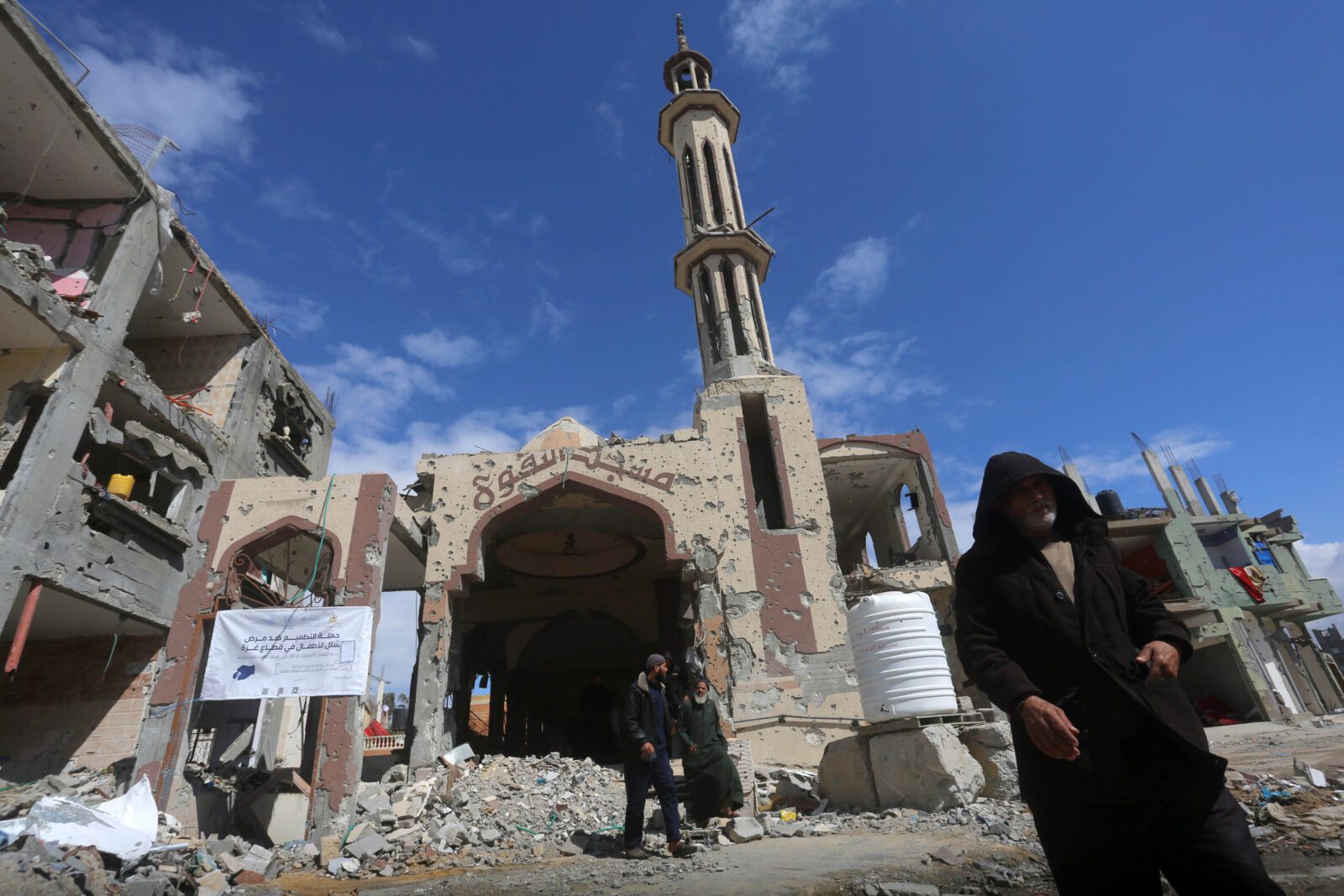 A man in black clothing walks past a mosque destroyed by airstrikes in Gaza.