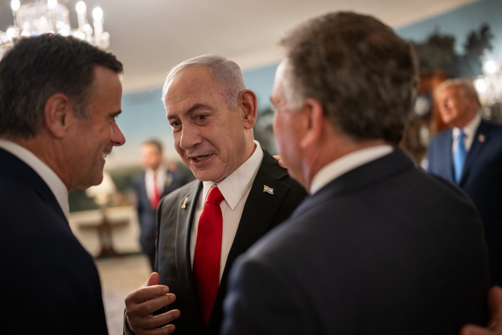 Israeli Prime Minister Benjamin Netanyahu leans in to speak with men in suits, during a visit to the White House.