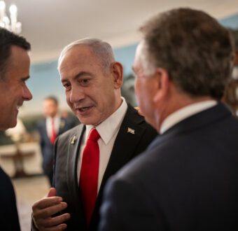 Israeli Prime Minister Benjamin Netanyahu leans in to speak with men in suits, during a visit to the White House.