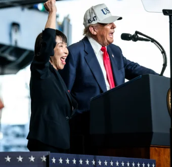 President Trump and Japanese Prime Minister Sanae Takaichi stand at a podium together, as Takaichi waves.