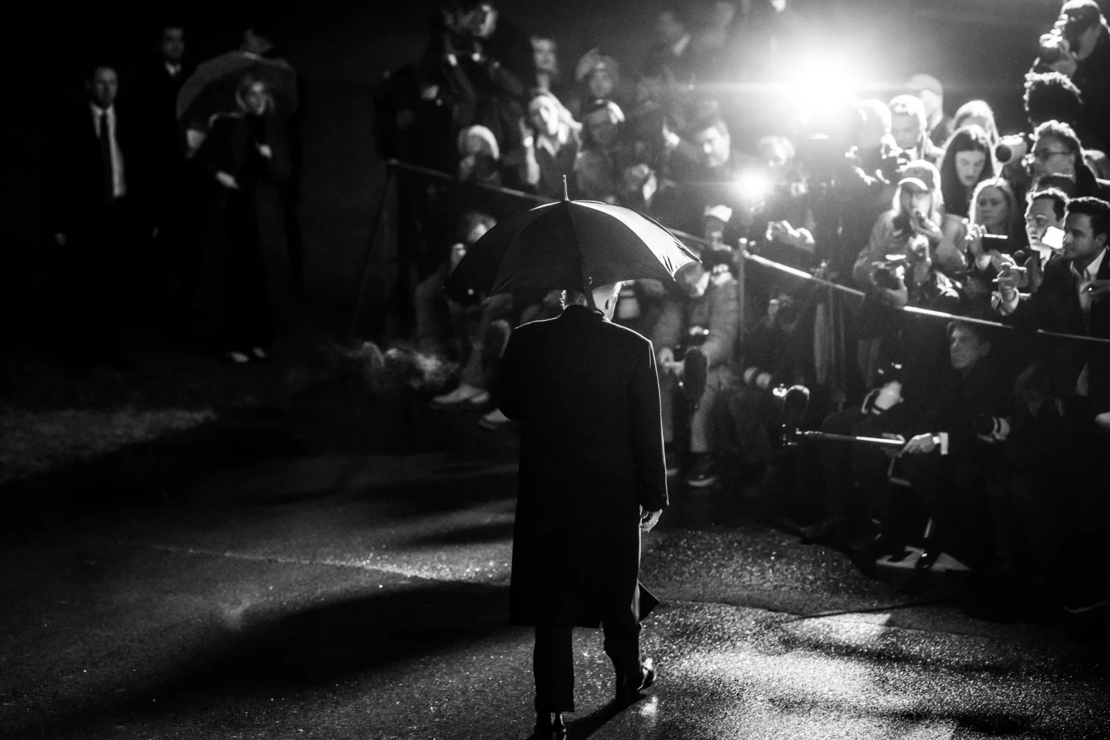 President Trump faces towards the flashing lights of the White House Press Pool cameras while holding an umbrella.