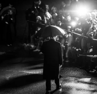 President Trump faces towards the flashing lights of the White House Press Pool cameras while holding an umbrella.