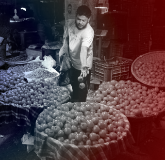 A man tosses a few tomatoes into a basket full of them in a street market.