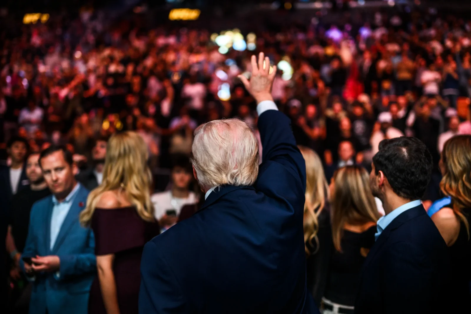 President Trump turns away from the camera, raising his hand to an audience.