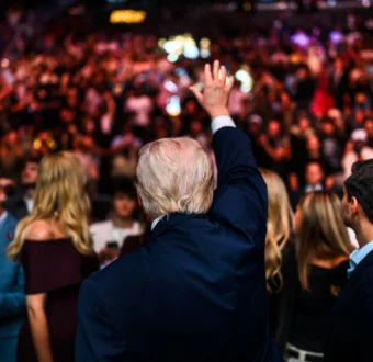 President Trump turns away from the camera, raising his hand to an audience.