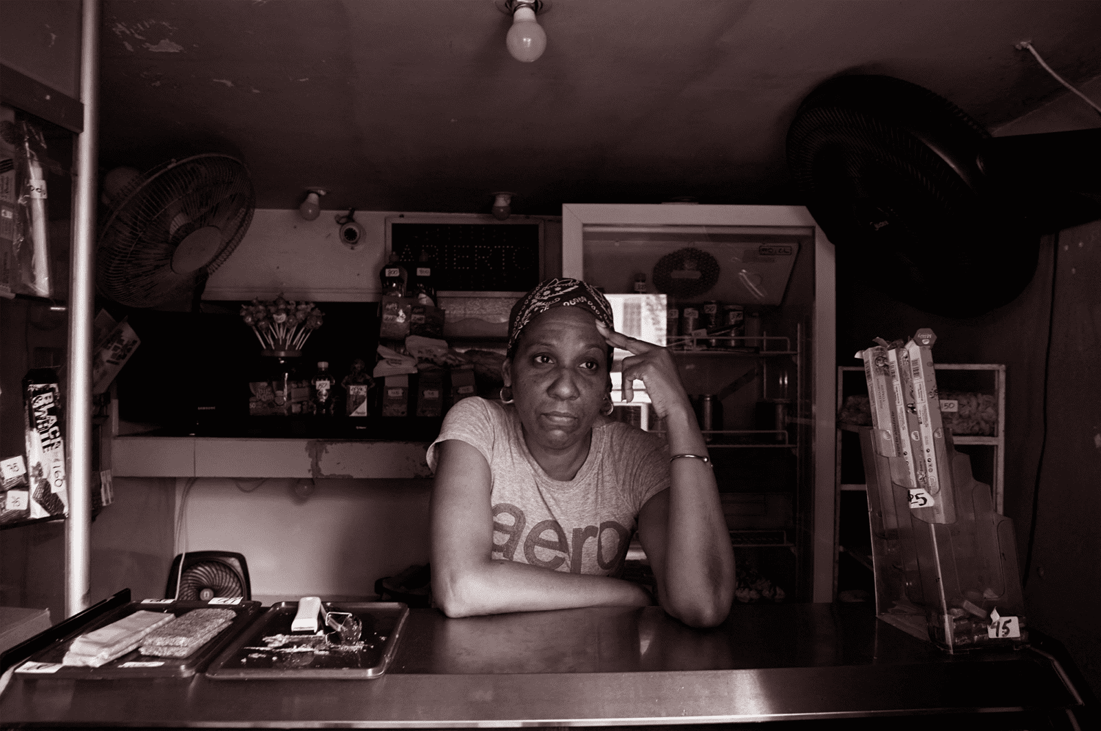 A woman leans against a shop counter, with her hand on her head.