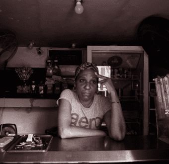 A woman leans against a shop counter, with her hand on her head.