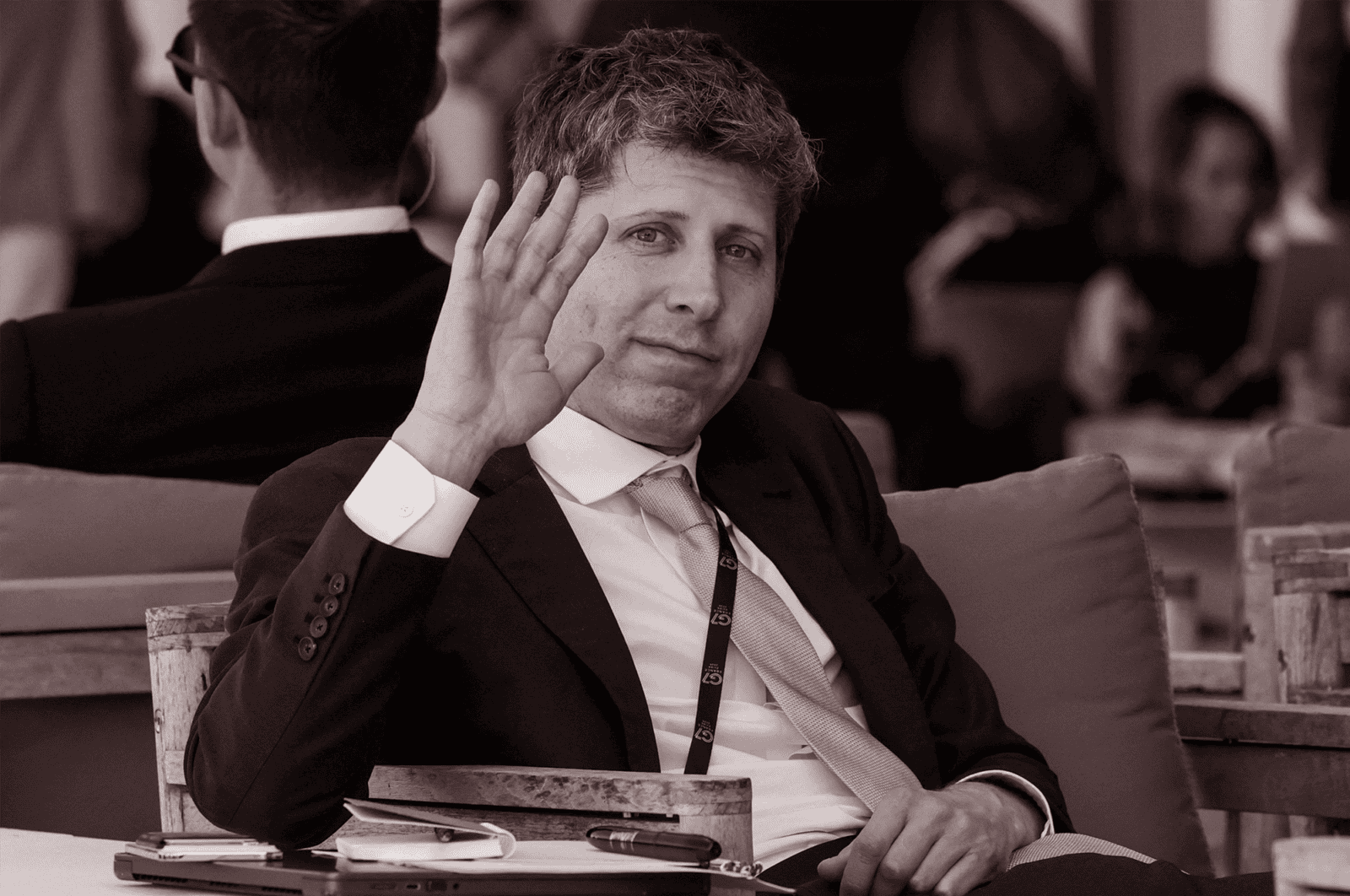 OpenAI CEO Sam Altman waves to camera seated at the G7 summit.