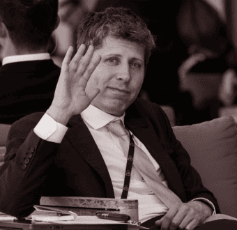 OpenAI CEO Sam Altman waves to camera seated at the G7 summit.